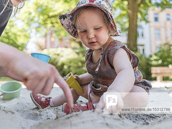 Porträt eines kleinen Mädchens mit seiner Mutter im Sandkasten auf dem Spielplatz