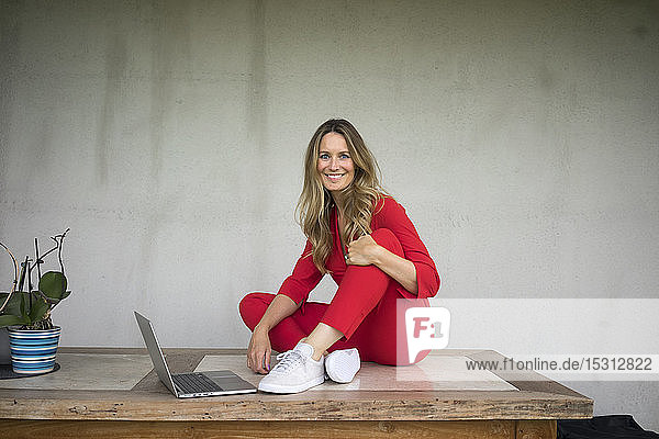 Smiling woman with laptop sitting on wooden table at home