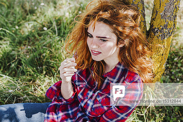 Portrait of redheaded woman having cigarette break under a tree