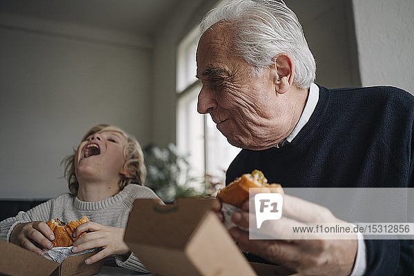 Happy grandfather and grandson eating burger together at home