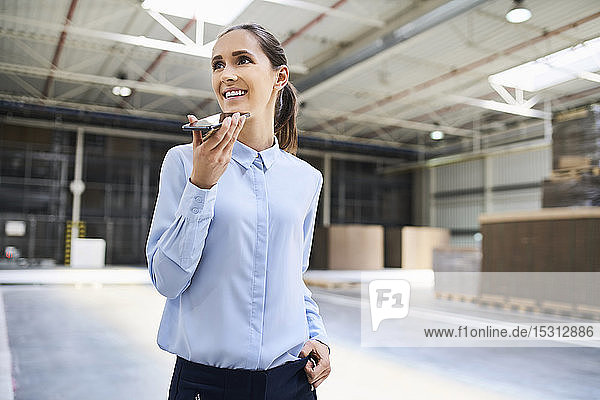 Smiling businesswoman using cell phone in a factory
