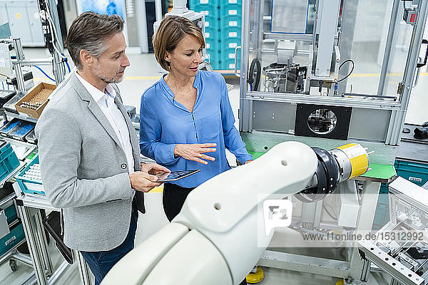 Geschäftsmann mit Tablette und Frau im Gespräch am Montageroboter in einer Fabrik