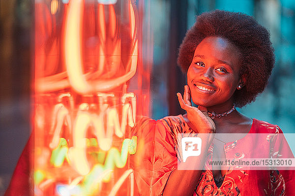 Lächelnde junge Frau steht neben Neonlicht