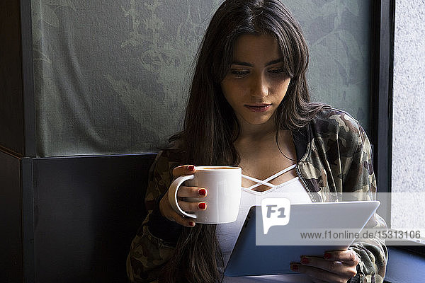 Junge Frau sitzt im Café mit einer Tasse Kaffee und benutzt Tabletten