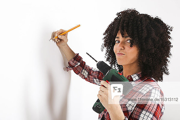 Frau mit tragbarem Bohrer  Markierung mit Bleistift an einer Wand