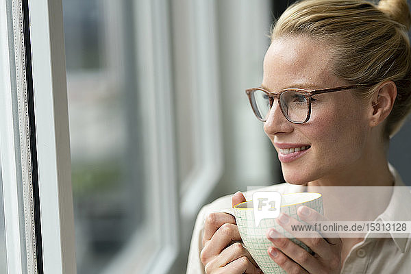 Junge Geschäftsfrau mit einer Tasse Kaffee  die aus dem Fenster schaut