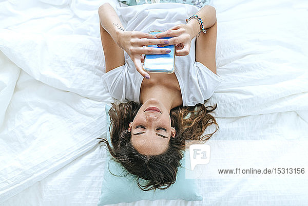 Draufsicht einer jungen Frau, die mit ihrem Handy im Bett liegt