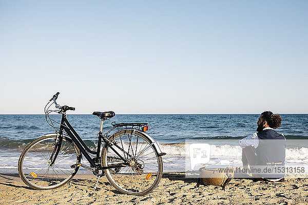 Gut gekleideter Mann mit seinem Fahrrad am Strand sitzend