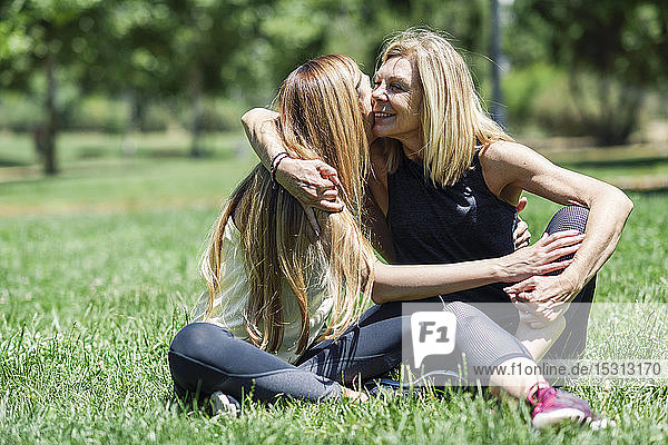 Sportliche reife Frau und ihre Tochter umarmen sich auf einer Wiese in einem Park