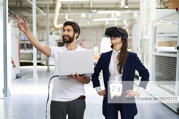 Mann mit Laptop und Geschäftsfrau mit VR-Brille in der Fabrik