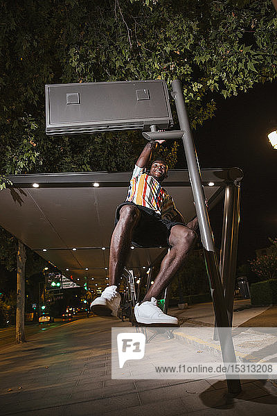 Verspielter junger Mann  der nachts in der Stadt an einem Straßenschild hängt