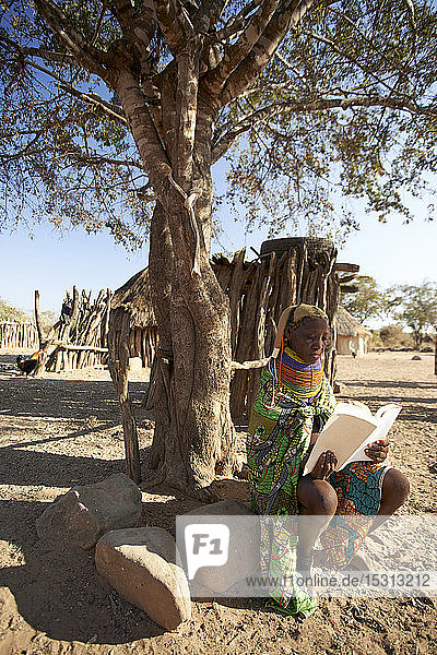 Traditional muhila woman  sitting under tree  reading a book  Kehamba  Chibia  Angola
