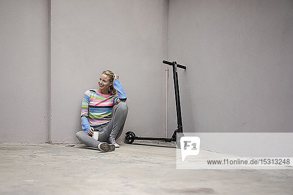 Young woman with electric scooter in a loft  sitting on floor  drinking coffee