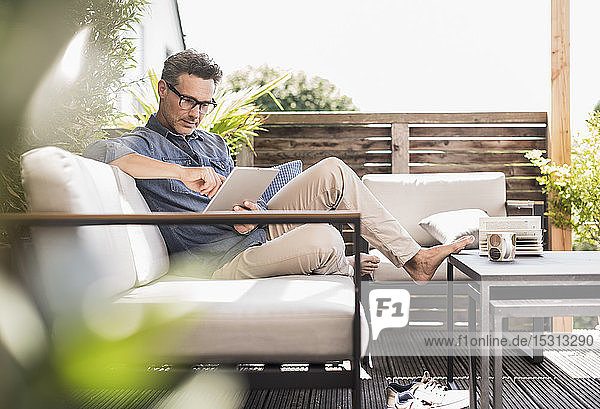 Mature man sitting on terrace using digital tablet