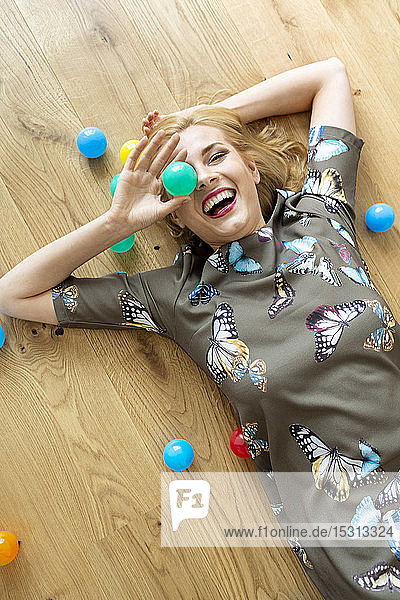 Lachende junge Frau mit bunten Bällen auf dem Boden liegend
