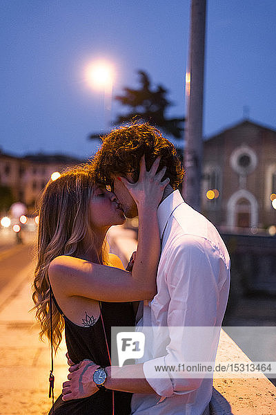 Zärtliches junges Paar küsst sich nachts auf einer Brücke  Verona  Italien