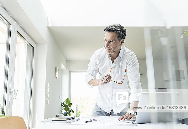 Architect working on blueprint in a bright office using laptop