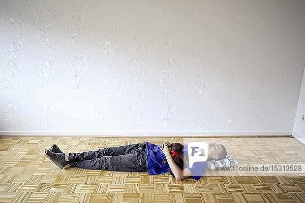 Junger Mann liegt in einer leeren Wohnung auf dem Boden und umarmt einen Teddybär