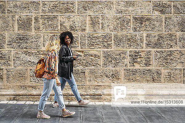 Multikulturelle glückliche Frauen  die in der Stadt spazieren gehen und ein Smartphone benutzen