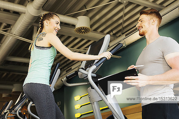 Young woman exercising on step machine in fitness gym with personal trainer
