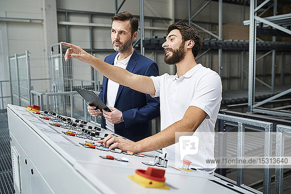 Geschäftsmann und Angestellter im Gespräch an einer Schalttafel in einer Fabrik