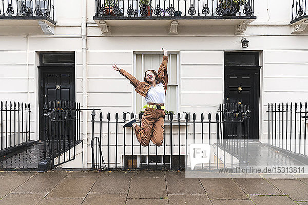 Unbeschwerte junge Frau springt vor Stadthäuser  London  UK