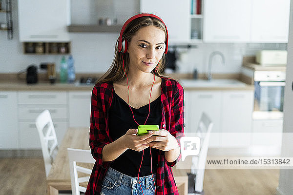 Porträt einer jungen Frau mit Handy und Kopfhörer zu Hause