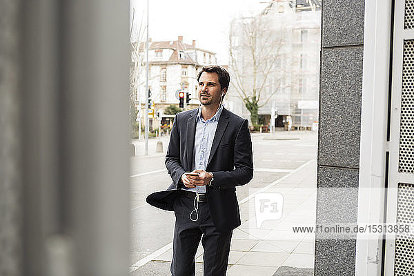 Portrait of businessman using earphones and mobile phone in the city