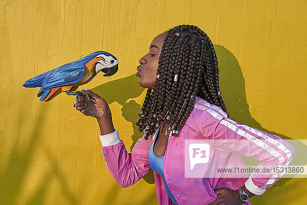 Frau küsst einen hölzernen Papagei auf einer gelben Wand