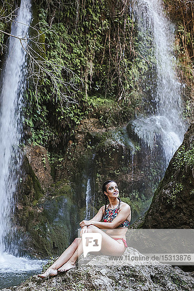 Junge Frau sitzt an einem Wasserfall