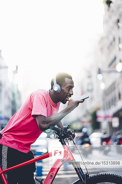 Junger Mann mit E-Fahrrad und Kopfhörer mit Smartphone in der Stadt