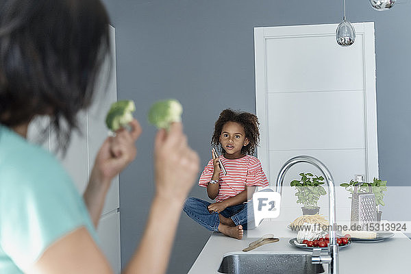 Mother showing broccoli to daughter in kitchen