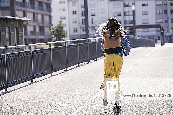Rear view of young woman riding electric scooter on a bridge
