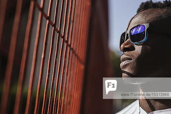 Serious young man at a fence wearing sunglasses