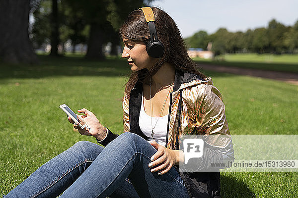 Porträt einer jungen Frau  die eine glänzende Jacke trägt und ein Smartphone und Kopfhörer benutzt
