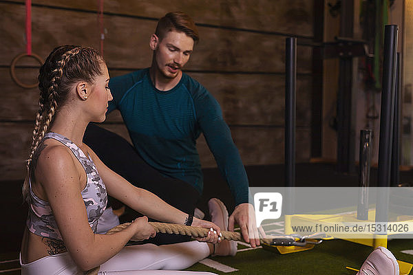 Junge Frau trainiert im Fitness-Studio mit einem persönlichen Trainer  der am Seil zieht