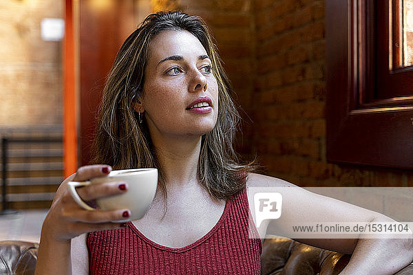 Porträt einer jungen Frau mit einer Tasse Kaffee  die aus dem Fenster schaut