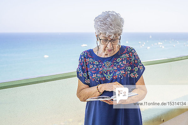 Ältere Frau liest ein Buch auf einer Terrasse