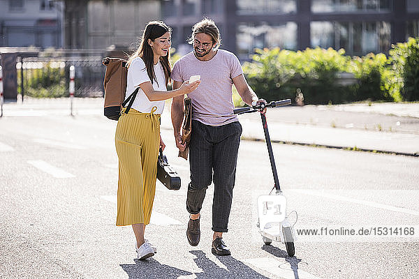 Young couple with electric scooter and smartphone walking on the street