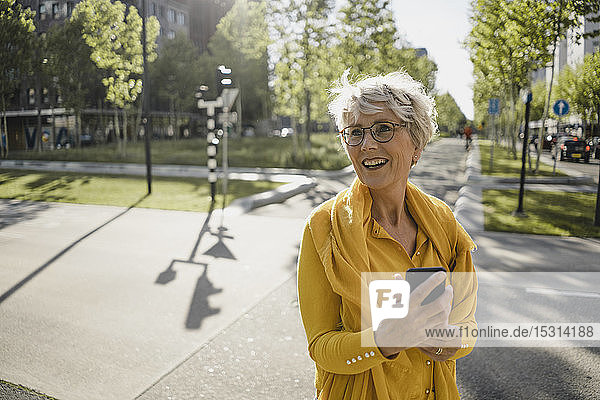 Porträt einer glücklichen reifen Frau mit Smartphone  die im Freien gelbe Kleidung trägt