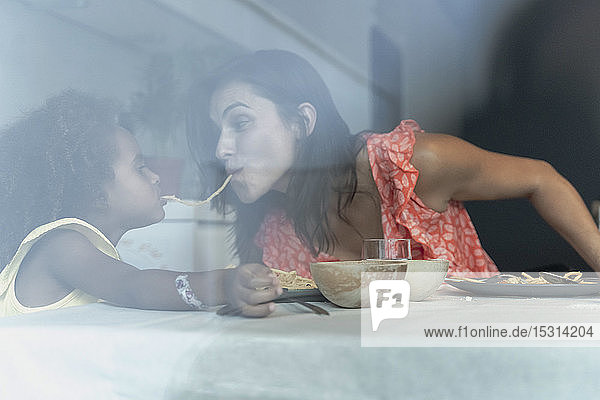Mother and daughter eating pasta at dining table sharing a spaghetti