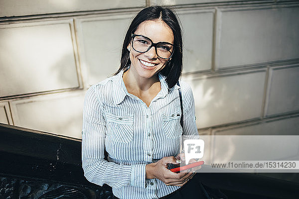 Porträt einer glücklichen jungen Geschäftsfrau mit Handy im Freien