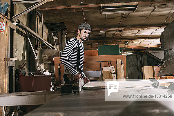 Carpenter at work with wooden board on a saw