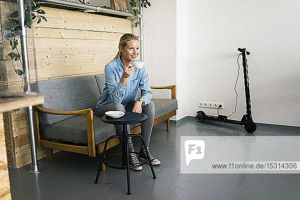 Young woman sitting on couch in a coffe shop  e-scooter charging in background