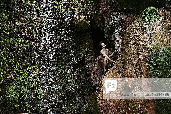 Barbusiger junger Mann klettert an einem Wasserfall