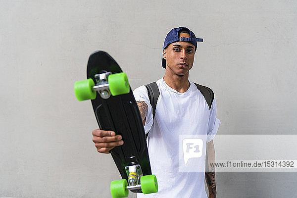 Portrait of tattooed young man with skateboard in front of grey background