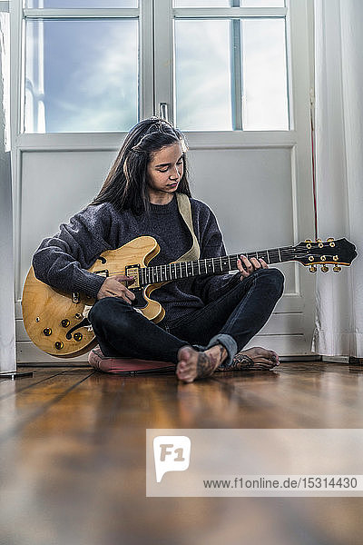 Junge Frau sitzt zu Hause auf dem Boden und spielt Gitarre