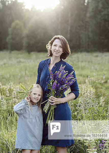 Porträt von Mutter und kleiner Tochter mit Lupinenbüschel auf einer Wiese