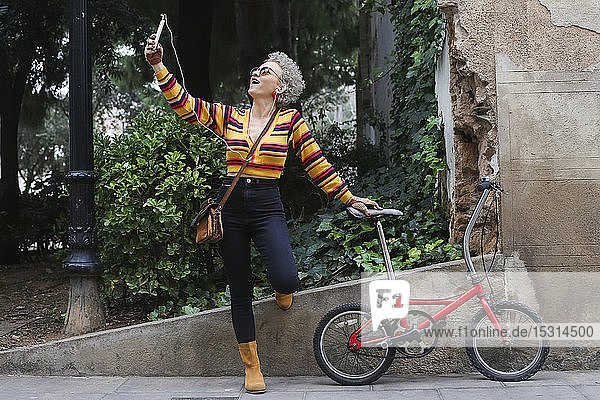 Modische reife Frau mit Fahrrad  die sich mit dem Smartphone selbstständig macht