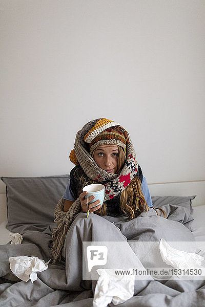 Kranke junge Frau  die zu Hause im Bett Tee trinkt